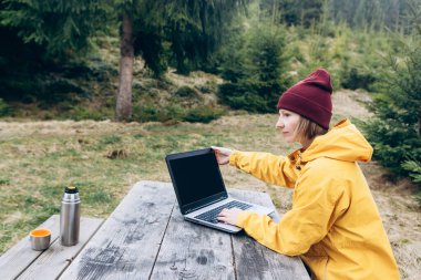 Dışarıda dizüstü bilgisayarda çalışan güzel doğayla çevrili bir kadın.