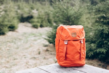 Hipster orange backpack. View from front tourist traveler bag with forest background. Travel outdoor concept