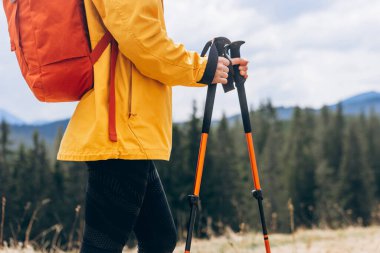 Close up Hiker with trekking poles goes against mountain landscape. Hiking and travel concept