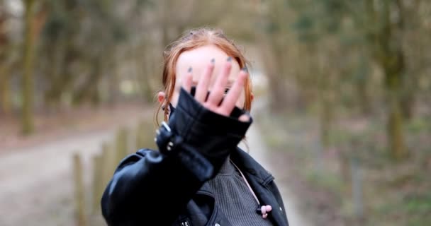 Mooi jong meisje of vrouw draagt gezichtsmasker om te beschermen tegen coronavirus uitbraak tweede golf van pandemie, op zoek naar camera buiten. roodharige student tonen hand omhoog voor privacy close-up — Stockvideo