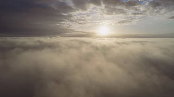 Vista aérea. Volando en la niebla, volar en la niebla sobre las nubes de la mañana temprano en el sol naciente. Cámara aérea grabada. Vuelo por encima de las nubes hacia el sol con las nubes de niebla flotando. Clima brumoso — Foto de Stock