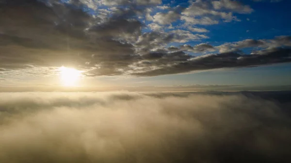 空中展望。霧の中で飛んで、上昇する太陽の下で早朝の雲の上に霧の中で飛ぶ。空中カメラ撮影。霧の雲が浮かんで太陽に向かって雲の上の飛行。霧の多い天気 — ストック写真