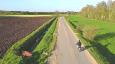 Bir motosikletçi toprak yolda turistik bir motosiklet sürüyor. Ufkun ötesindeki yeşil alanlar. Yaz günü. Açık hava eğlencesi konsepti. Hafta sonları. Tatil ve aşırı hobiler. Hava görünümü