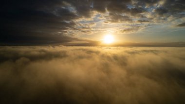 Hava görüntüsü. Sis içinde uçmak, güneşin doğuşundaki sabah bulutlarının üzerinde uçmak. Hava kamerası görüntüsü. Bulutların üzerinden güneşe doğru uçarken sis bulutları yüzüyor. Sisli hava