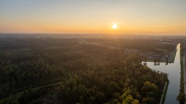 Yeşil çalıları ve renkli gökyüzü olan bir nehrin üzerinde güzel bir gün batımı.