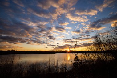 Önünde ağaç siluetleri olan güzel mavi bir göl dramatik bir günbatımı gökyüzünün altında.
