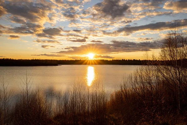 Un hermoso lago azul con algunas siluetas de árboles en primer plano bajo un dramático cielo al atardecer — Foto de Stock