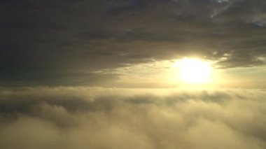 Hava görüntüsü. Sis içinde uçmak, güneşin doğuşundaki sabah bulutlarının üzerinde uçmak. Hava kamerası görüntüsü. Bulutların üzerinden güneşe doğru uçarken sis bulutları yüzüyor. Sisli hava