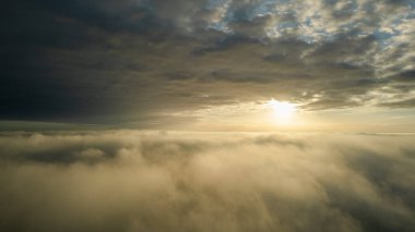 Hava görüntüsü. Sis içinde uçmak, güneşin doğuşundaki sabah bulutlarının üzerinde uçmak. Hava kamerası görüntüsü. Bulutların üzerinden güneşe doğru uçarken sis bulutları yüzüyor. Sisli hava
