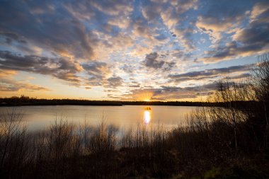 Önünde ağaç siluetleri olan güzel mavi bir göl dramatik bir günbatımı gökyüzünün altında.