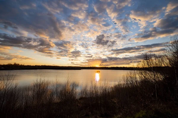 Önünde ağaç siluetleri olan güzel mavi bir göl dramatik bir günbatımı gökyüzünün altında.