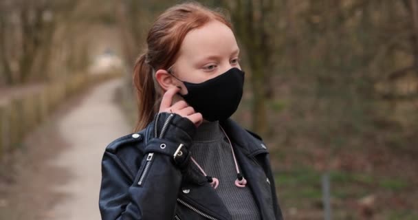 Quítate una mascarilla. Una hermosa pelirroja adolescente feliz vestida con ropa negra se quita la mascarilla y comienza a respirar en el bosque. Un concepto del fin de la cuarentena de la corona. — Vídeo de stock