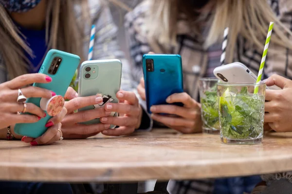 Закрытие рук многорасовой группы из четырех женщин, использующих смартфоны за столом в кафе в городе с коктейлями и напитками — стоковое фото
