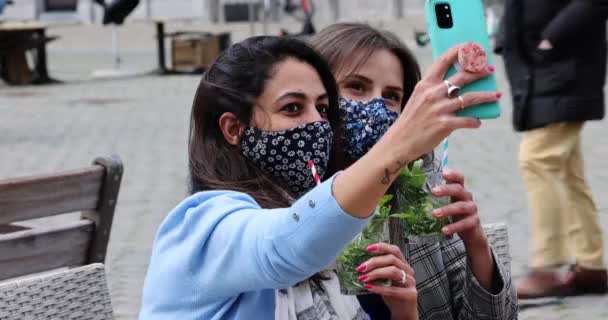 Antwerpen, Belgien, 21. Mai 2021, multirassische junge Freundinnen tragen Gesichtsmaske, während sie ein Selfie mit der Handy-Kamera machen, während sie auf der Terrasse eines Cafés in der Stadt Cocktails trinken. — Stockvideo