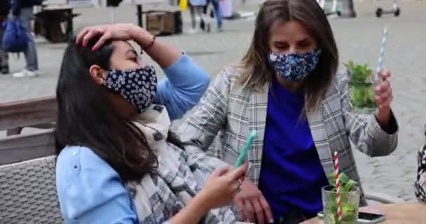 2021年5月21日，比利时安特卫普，多种族年轻女性朋友在城市一家咖啡馆的阳台上喝鸡尾酒时，带着面具，用手机摄像头自拍 — 图库视频影像