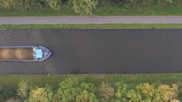 Vista aérea 4K de arriba hacia abajo Vista de pájaro con un dron de vía navegable con una barcaza o buque de carga de carga navegando a través de la zona verde natural de orest y campo de cultivo — Vídeos de Stock