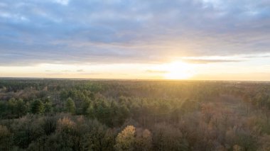 Yeşil çalıları ve renkli gökyüzü olan bir nehrin üzerinde güzel bir gün batımı.