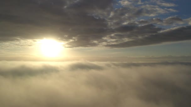 空中展望。霧の中で飛んで、上昇する太陽の下で早朝の雲の上に霧の中で飛ぶ。空中カメラ撮影。霧の雲が浮かんで太陽に向かって雲の上の飛行。霧の多い天気 — ストック動画