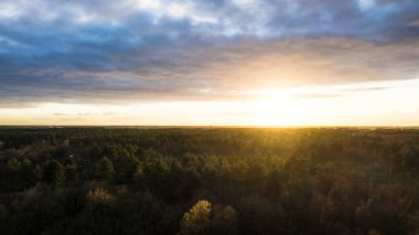 Yeşil çalıları ve renkli gökyüzü olan bir nehrin üzerinde güzel bir gün batımı.