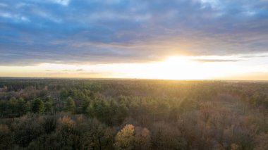 Yeşil çalıları ve renkli gökyüzü olan bir nehrin üzerinde güzel bir gün batımı.