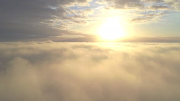 Vue Aérienne. Voler dans le brouillard, voler dans la brume au-dessus des nuages tôt le matin sous le soleil levant. Caméra aérienne prise. Vol au-dessus des nuages vers le soleil avec les nuages brumeux flottant par. Météo sinistre — Video