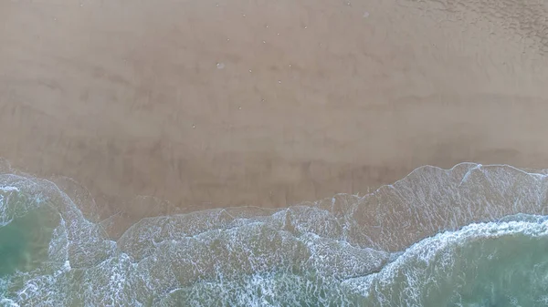 Aerial drone view perpendicular to the blue waves crashing on the sandy beach at the coast. The impact with wet wax creates white foam. The winter beach is empty. — Φωτογραφία Αρχείου