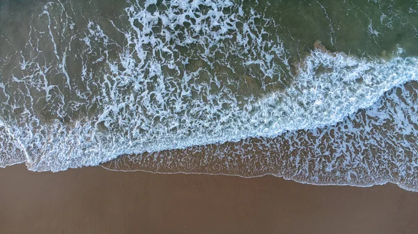 Letecký bezpilotní letoun pohled kolmo na modré vlny narážející na písečnou pláž na pobřeží. Náraz mokrým voskem vytváří bílou pěnu. Zimní pláž je prázdná. — Stock fotografie