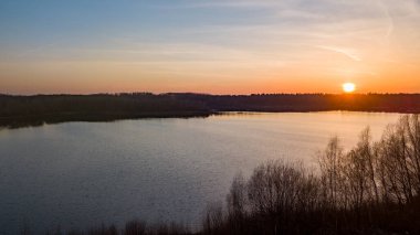 Göl kıyısında dramatik ve renkli bir gün batımının insansız hava aracı tarafından çekilen hava görüntüsü. Doğa manzarası. Avrupa 'da doğa. Yansıma, mavi gökyüzü ve sarı güneş ışığı. Gün doğumunda manzara veya