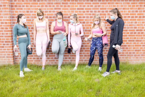 Profesionales atletas femeninos charlando y beber agua en un descanso del entrenamiento en el fondo de la pared de ladrillo usando mascarilla. Deporte durante cuarentena de pandemia mundial de coronavirus. Joven —  Fotos de Stock