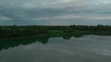 Büyük göl, tarım arazisi ve ormanın üzerinde gün batımı olan insansız hava aracı manzaralı güzel bir video..