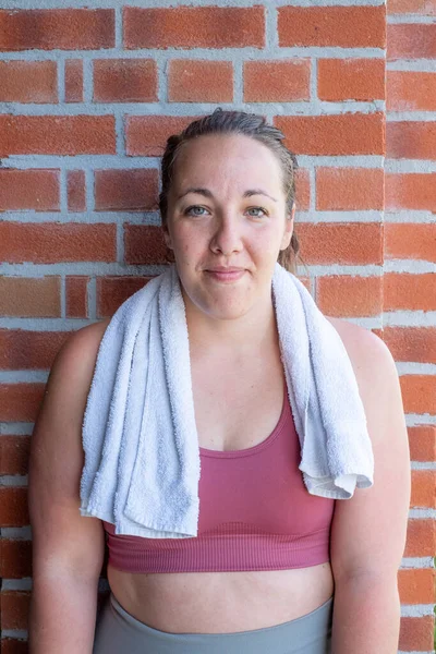 Full body portrait of an attractive sexy young sporty woman in sports clothing with towel around neck resting after a workout — Stock Photo, Image