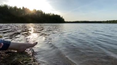 Gölün sahilinde suyun içinde güzel kadın bacakları. Gölde yaz tatili. Sahilde rahatla. Dalgalı su plajı. Güneş banyosu. Neşeli kadın ayakları