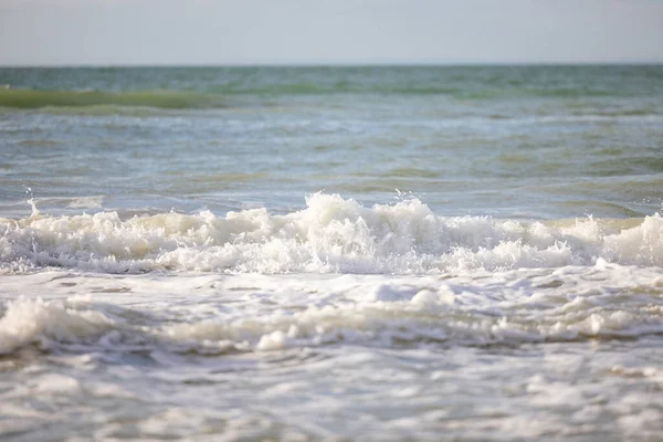 Rozbijające się fale okrążające piaszczystą plażę jeden po drugim pod błękitnym niebem zachodu słońca, selektywna ostrość. — Zdjęcie stockowe