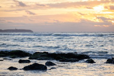 Kayalık bir kumsalda gün batımı. Sahilde büyük taşlarla turuncu gün batımı. Deniz günbatımının arka planında güzel bir dokusu olan büyük taşlar. Kayalık deniz kıyısında akşam manzarası.