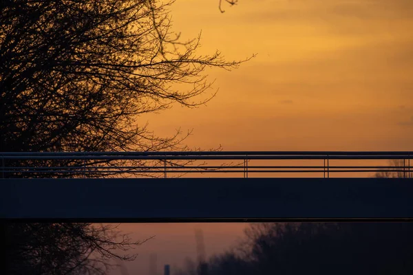 Detalle del puente peatonal colgante largo o pasarela sobre el canal en Rijkevorsel, Amberes, Bélgica, contra un cielo naranja dramático del amanecer en invierno — Foto de Stock