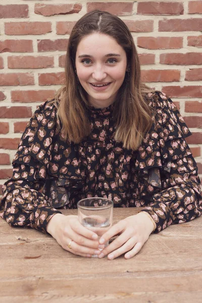 Güzel gülümseyen genç bir kadın sabah uyandıktan sonra elinde bir bardak saf su tutuyor. Genç kız, şeffaf bir bardak temiz su içerek vücut sağlığı için su dengesini sağlıyor. Uzun web pankartı.