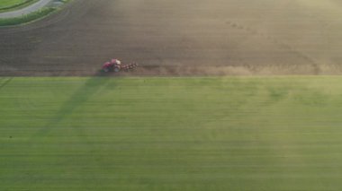 Aerial drone view of a tractor with cultivator plowing field in the early morning fog lit up the golden sunrise. Tractor disk harrow on ploughing a soil. Planting in farmland. Sowing seed on plowed