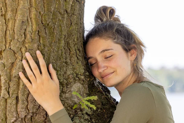 Mutlu bir ifadeyle büyük bir ağaca sarılmış tatmin olmuş genç bir kadın ve gözleri ormanı kurtarma, ormansızlaşmayı, doğayı ve doğayı birbirine bağlayan dünyalar gününü durdurma konseptiyle kapalı.