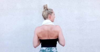 Beden Eğitimi Kafkasyalı spor giyinmiş, saçları boynuna toka dolamış ve elleriyle spor salonunda ayakta duran bir kadının yarı vücut arkası görüntüsü. Arkaplan duvarında