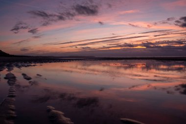 Güzel, dramatik bir altın gün batımı. Güzel bir Fransız sahilinin üzerinde küçük kara bulutlar ve kıyıdan gelen küçük dalgalar. Yüksek kalite fotoğraf