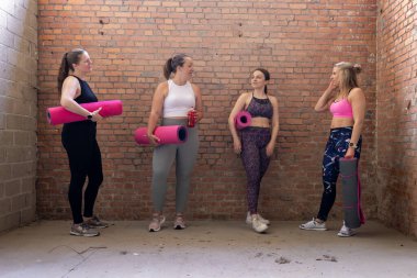 Farklı vücut biçimlerinde çeşitli çekici ve sportif kadınlardan oluşan bir grup spor salonunda beklerken bir araya geldiler ve konuştular. Endüstriyel tuğla arka plan. Yüksek kalite fotoğraf