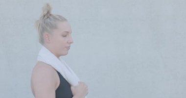Portrait of an attractive sexy and vivacious young caucasian blonde sporty woman in sports clothing with towel around neck resting after a workout. High quality 4k footage