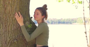 Mutlu bir ifadeyle büyük bir ağaca sarılmış tatmin olmuş genç bir kadın ve gözleri ormanı kurtarma, ormansızlaşmayı, doğayı ve doğayı birbirine bağlayan dünyalar gününü durdurma konseptiyle kapalı.