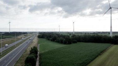 Brecht, Belgium, 6th of July, 2022, Panoramic aerial drone view of wind farm or wind park, with high wind turbines for generation electricity with the motorway with few cars and railroad next to it