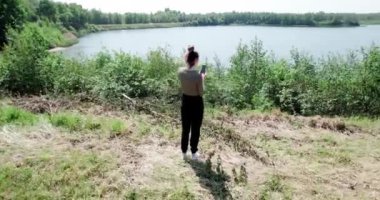 Kafkasyalı güzel kadın, yeşil orman göl kenarında cep telefonuyla işaret fişeğiyle fotoğraf çekiyor. Yüksek kalite 4k görüntü