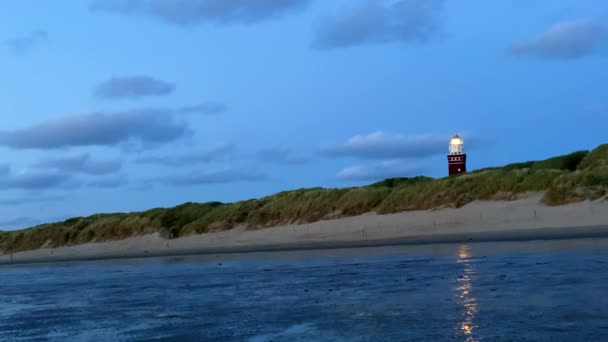 夕日の空に対して穏やかな海で砂丘に高い灯台のシルエット 高品質4Kズーム映像 — ストック動画