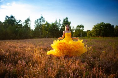 Beautiful and sensual young caucasian woman wearing a yellow evening dress outside in a natural setting over a heather and forest background. High quality photo