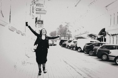 Deri ceketli gülümseyen bir kızın portresi. Şehrin sokaklarında poz veren uzun siyah bir elbise. Tarz ve moda konsepti. Kulaklarında küpeleri olan mutlu bir kız..