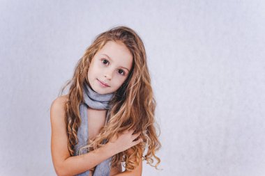Beyaz arka planda poz veren gri elbiseli, uzun kıvırcık saçlı güzel bir kız. Büyük kahverengi gözlü şirin bir kızın portresi..