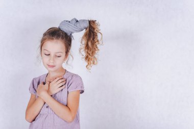 Uzun siyah saçlı, gri elbiseli, atkuyruklu şirin bir kız stüdyoda beyaz bir arka planda poz veriyor. Çocuk beyaz bir arkaplanda izole edilmiş. Kıvırcık saçlı bir çocuk. Sıra dışı bir saç stili olan bir kız..